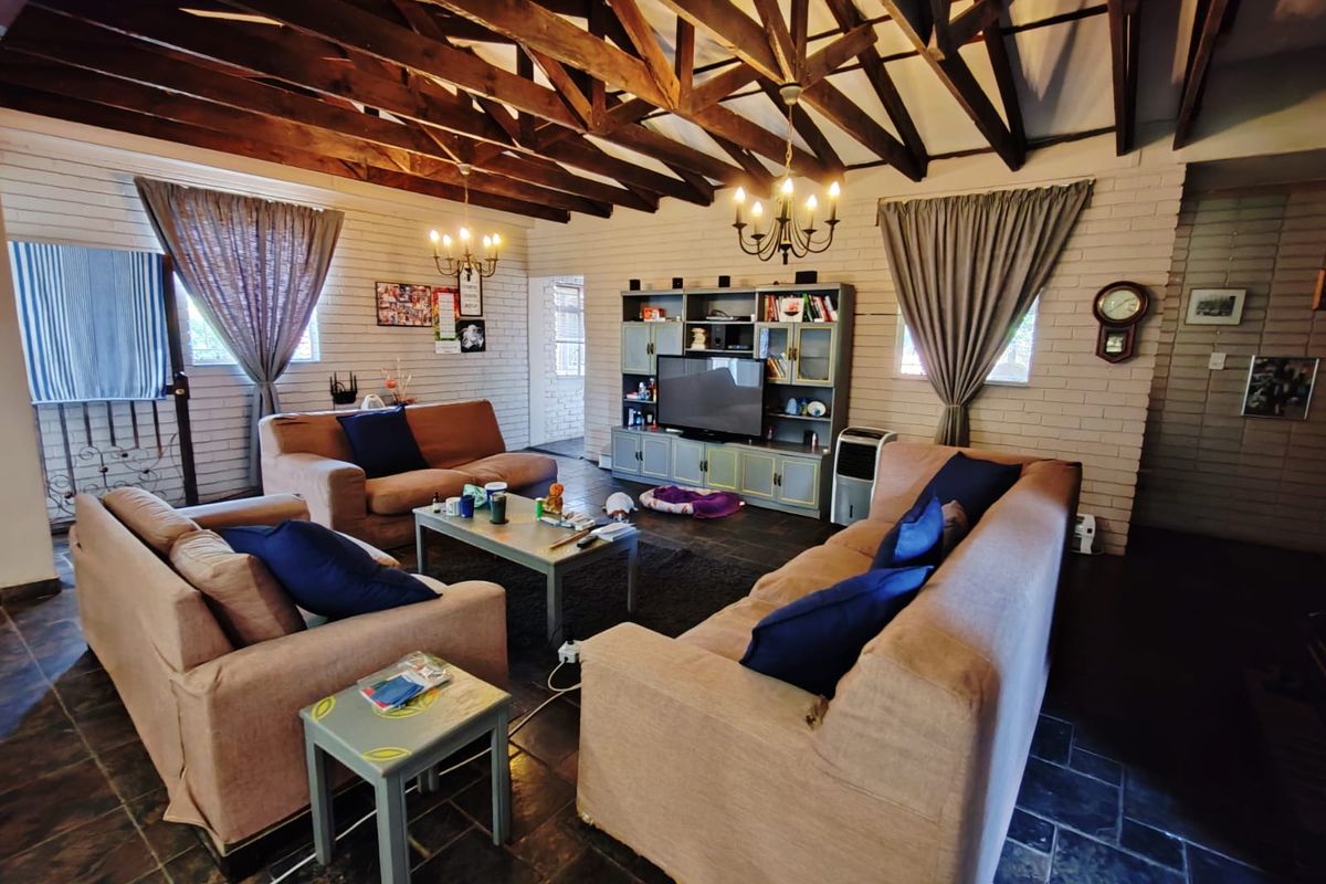 Spacious living room featuring exposed timber roof trusses, painted brick walls, and dark slate tile flooring, creating a rustic and inviting atmosphere.