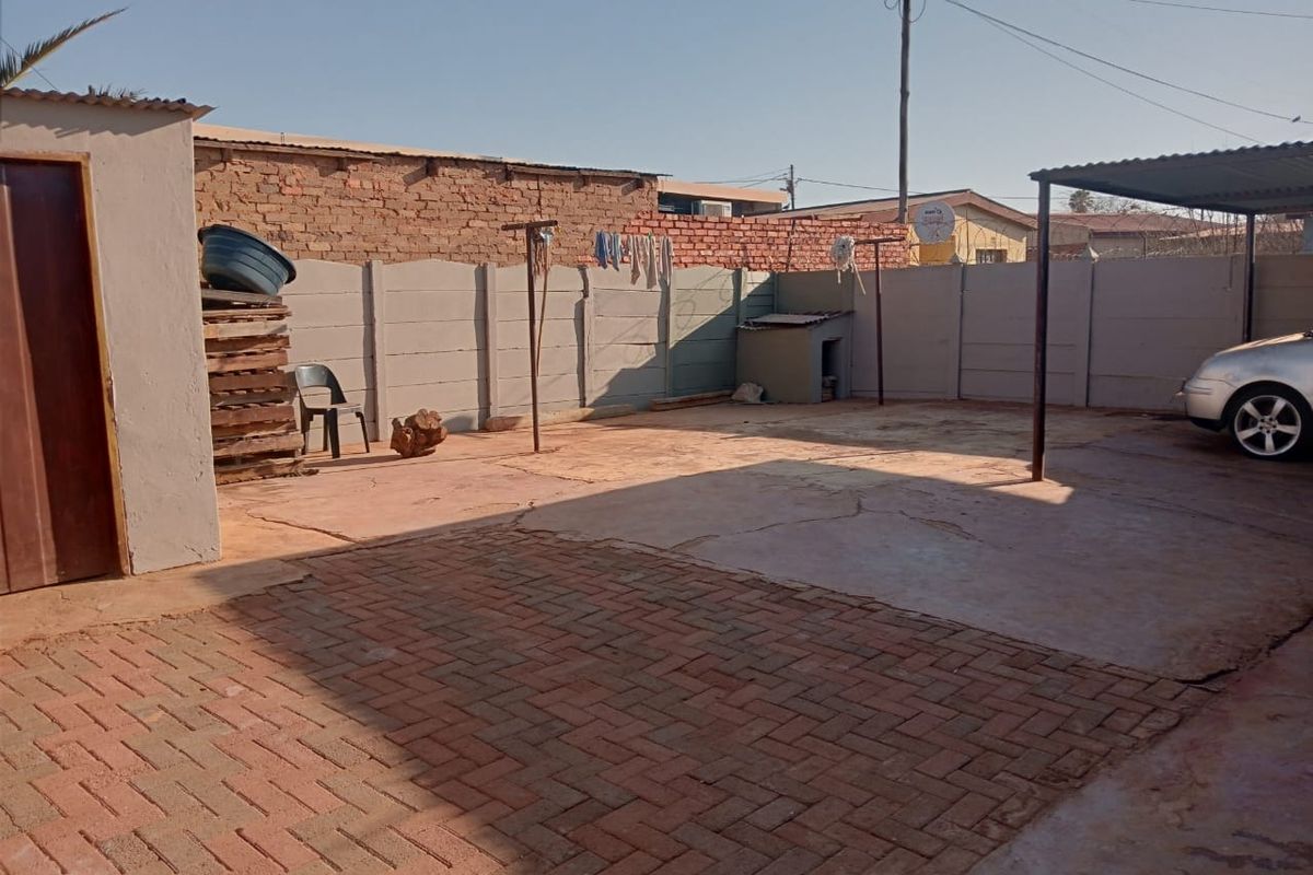 A paved rear courtyard area featuring a carport structure, concrete boundary walls, and a brick-paved section, providing functional outdoor space.