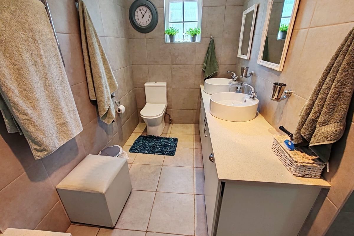 A well-maintained bathroom featuring a double vanity with vessel sinks, tiled walls and flooring, and a modern toilet.