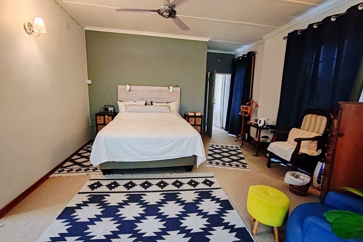 Spacious bedroom featuring a ceiling fan, wall-mounted lighting, and neutral carpeting, offering a comfortable and functional living space.
