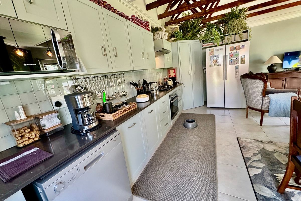 A well-maintained kitchen featuring sage green cabinetry, dark countertops, tiled backsplash, and exposed timber ceiling beams, creating a warm and functional cooking space.
