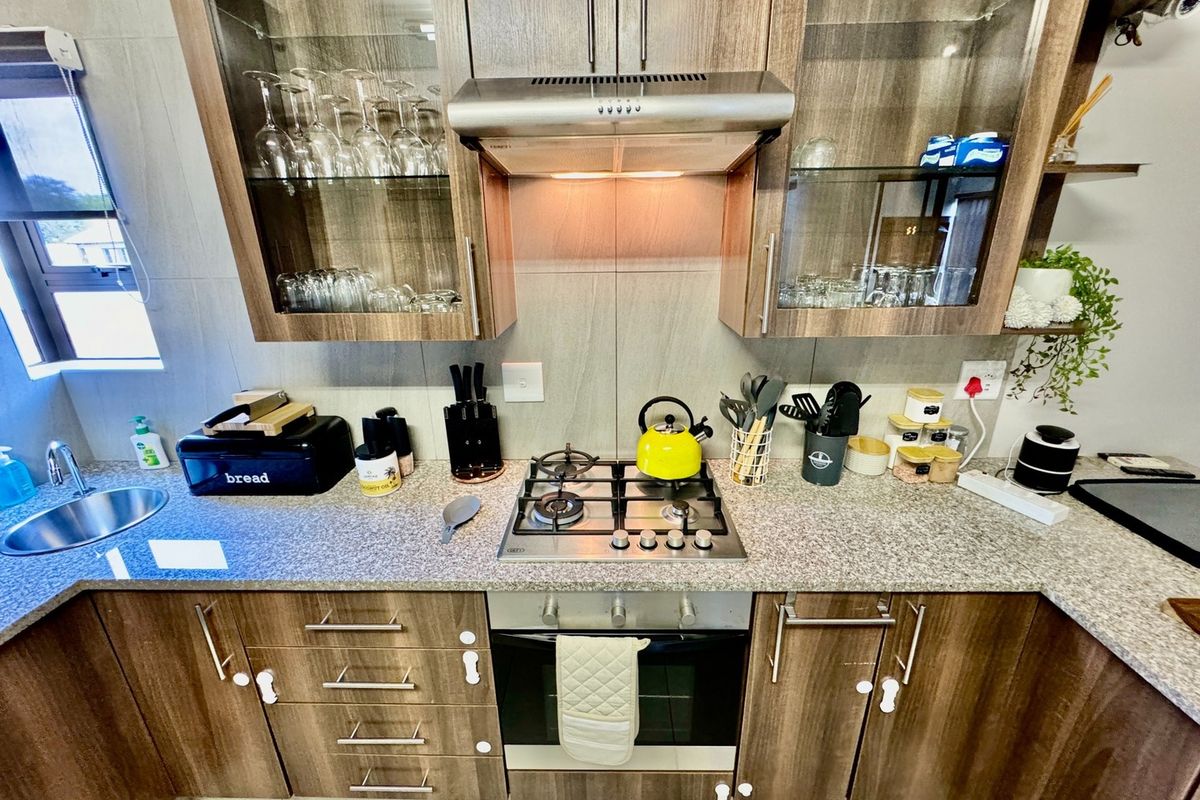 A well-maintained kitchen featuring wood-finish cabinetry, granite countertops, a built-in gas hob, an under-counter oven, and a stainless steel extractor fan.