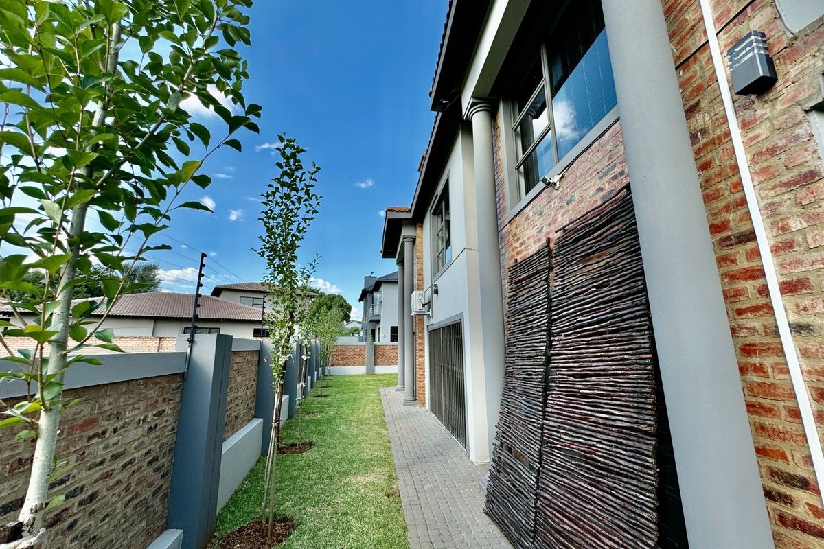 A side garden pathway featuring brick paving, manicured lawn, and a brick boundary wall with integrated electric fencing.