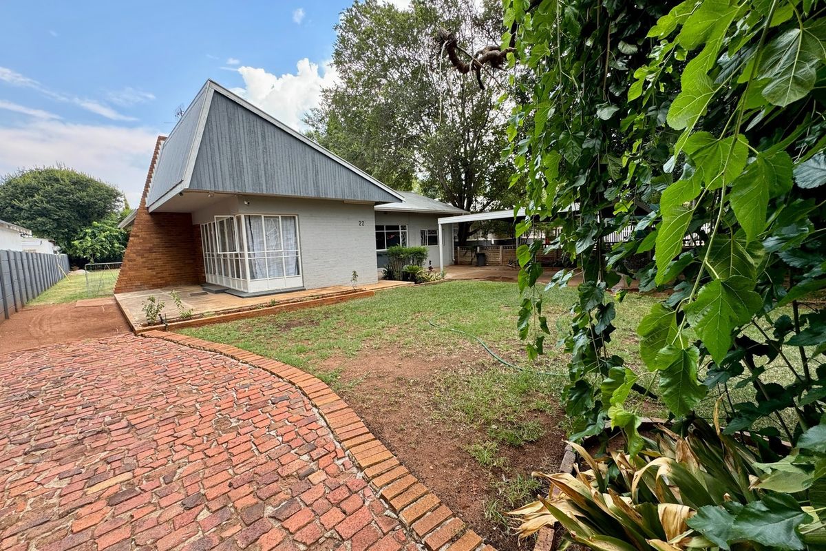 Rear view of the house featuring a unique A-frame architectural design, brick paving, and a spacious garden area.