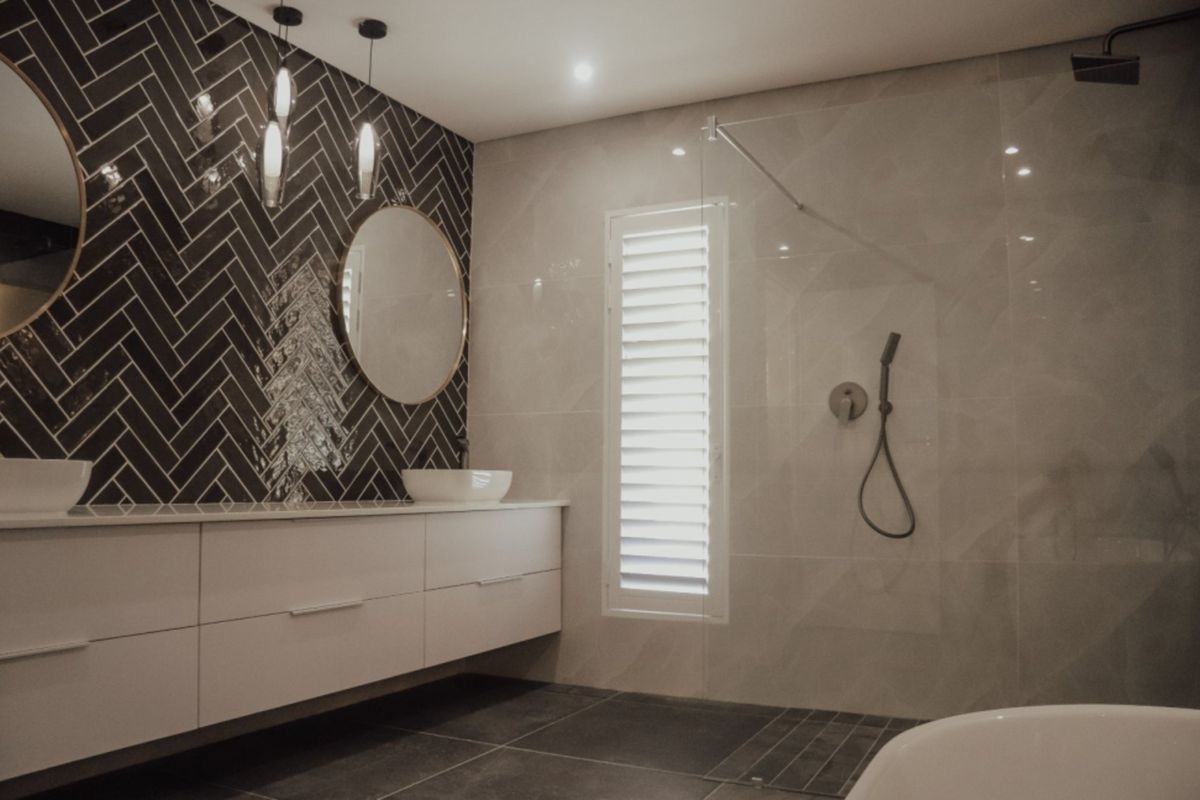 Modern bathroom featuring a floating vanity, herringbone tiled feature wall, walk-in glass shower, and plantation shutters.