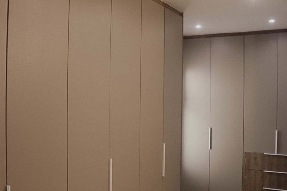 A modern bedroom featuring extensive floor-to-ceiling built-in cabinetry with sleek handles and integrated shelving, complemented by wood-look flooring and recessed ceiling lighting.