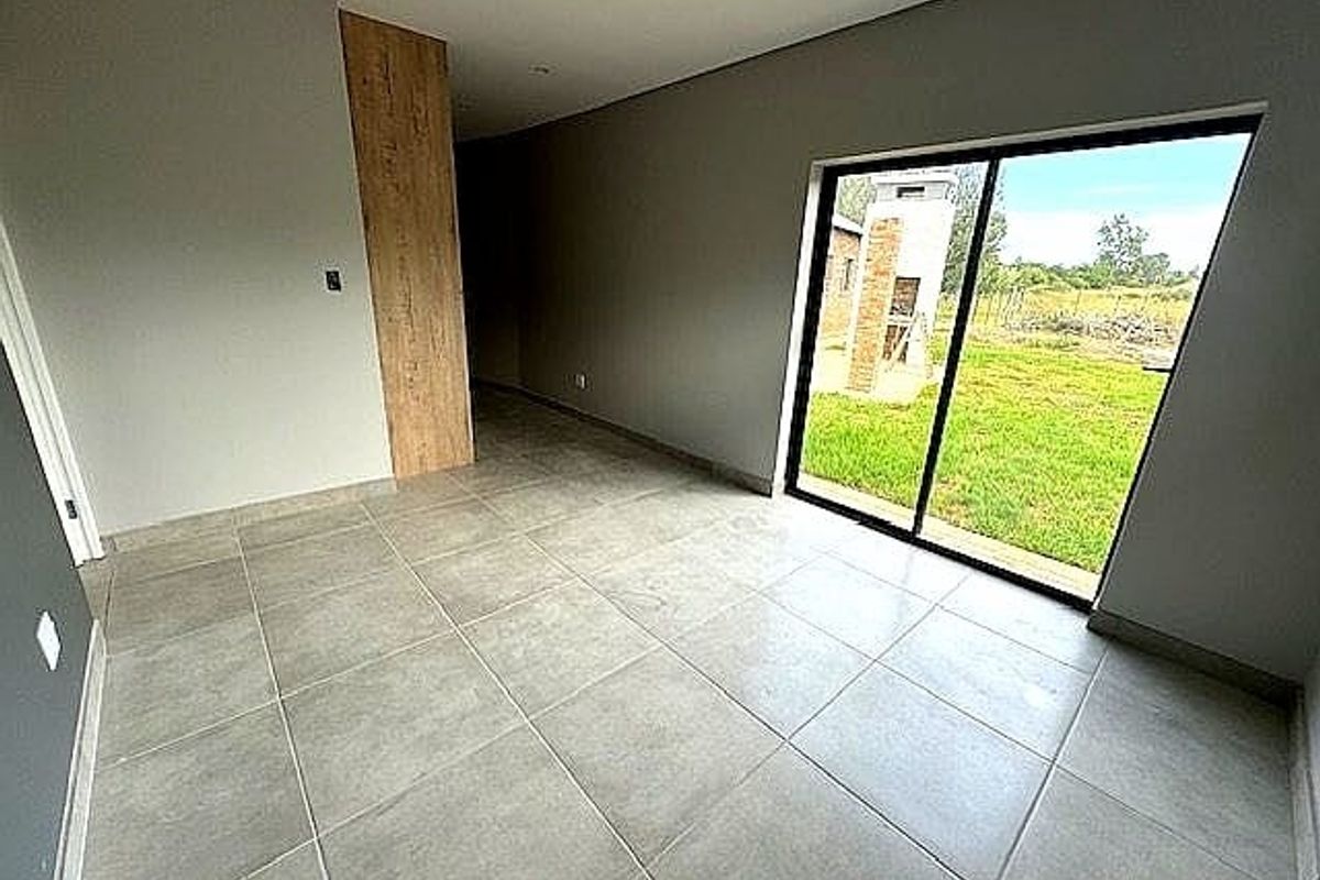 A bright, modern living area featuring large format floor tiles, recessed ceiling lighting, and a sliding glass door providing direct access to the garden.