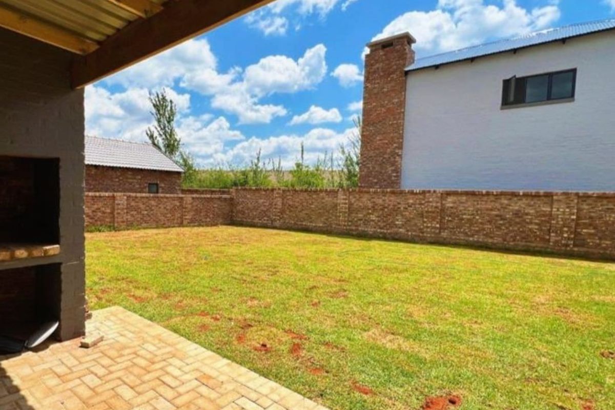 A spacious backyard featuring a paved patio area with a built-in braai, enclosed by a brick perimeter wall.
