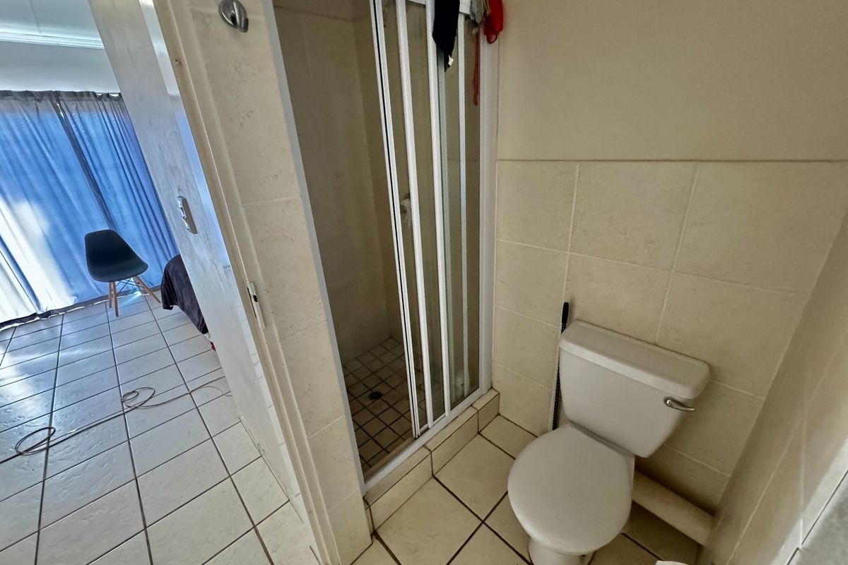 A functional bathroom featuring a shower cubicle with a folding door and a standard toilet, finished with neutral wall and floor tiling.