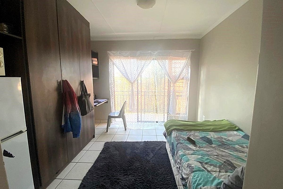 A bedroom featuring built-in wooden cupboards, tiled flooring, and a sliding door leading to a balcony.