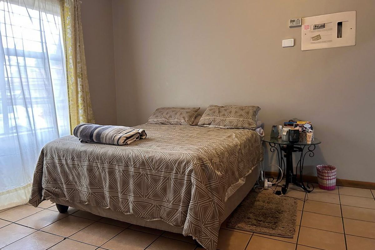 A bedroom featuring ceramic floor tiles, a wall-mounted electrical distribution board, and a thermostat, providing a functional living space.