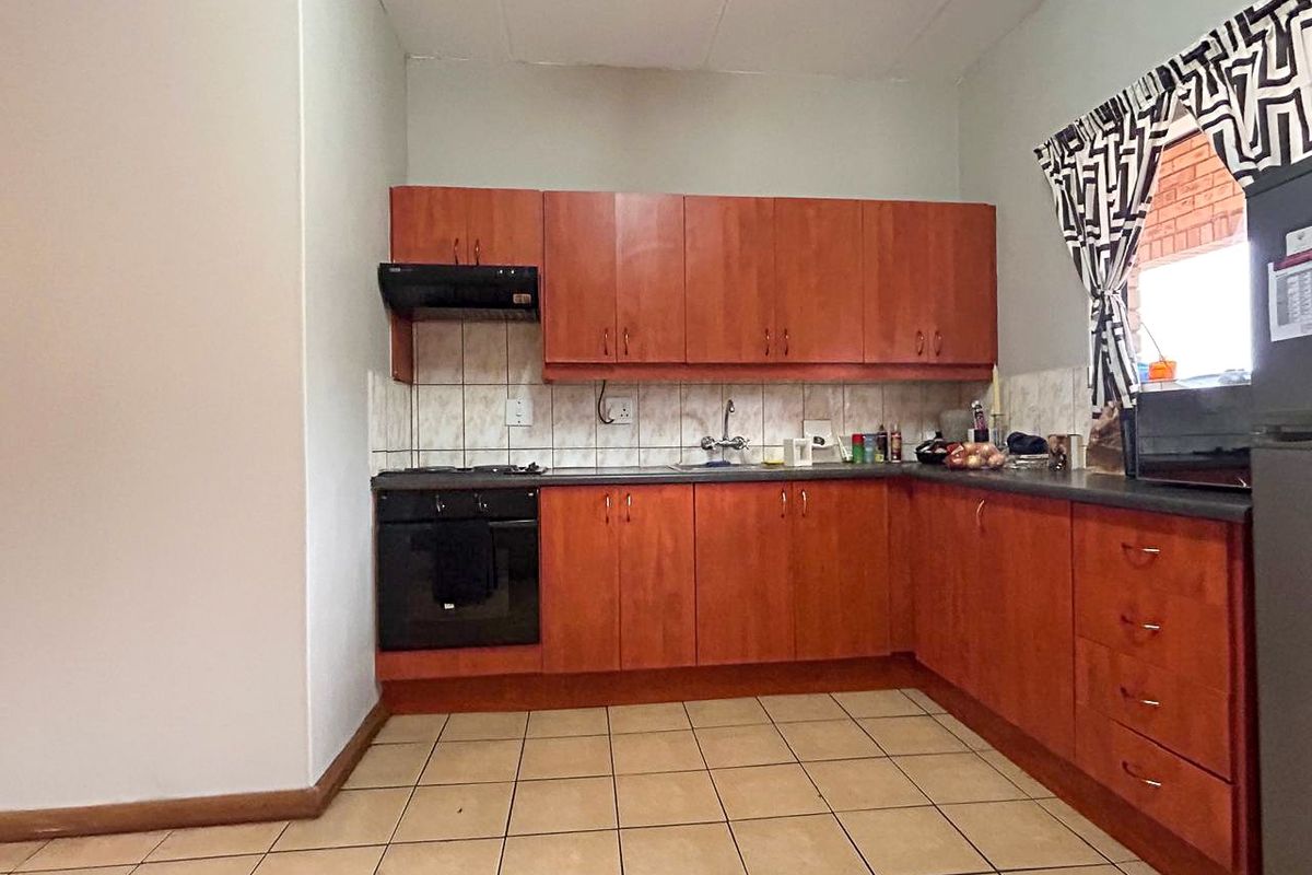 A functional kitchen featuring wood-look cabinetry, built-in oven, hob, extractor fan, and tiled flooring, offering a practical layout for daily meal preparation.