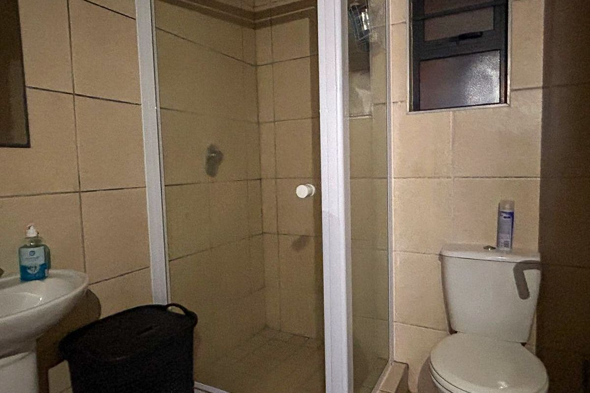 A compact bathroom featuring a corner shower enclosure, pedestal basin, and standard toilet with tiled walls and flooring.