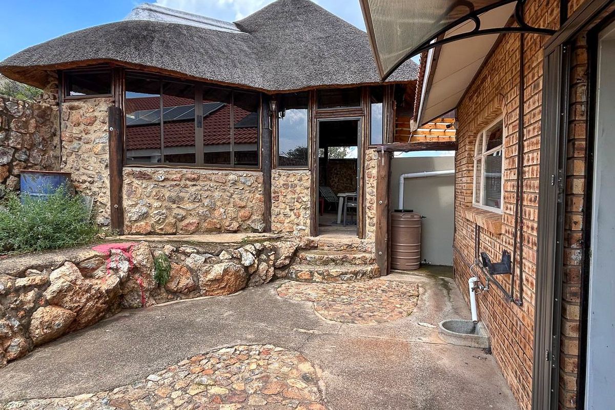 A rustic exterior rear courtyard featuring natural stone walling, a thatched roof structure, and paved flooring with integrated drainage.