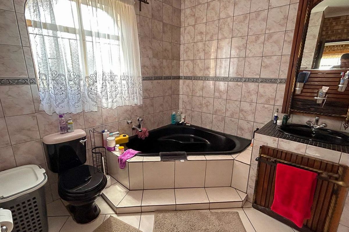 A dated bathroom featuring a corner bathtub, black toilet, and vanity unit with tiled walls and flooring.