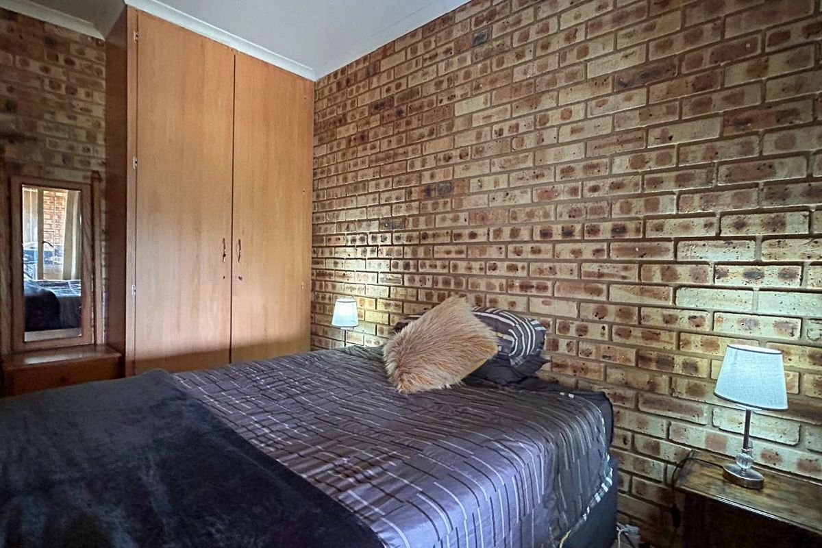 A bedroom featuring a prominent exposed brick feature wall and built-in wooden cabinetry.