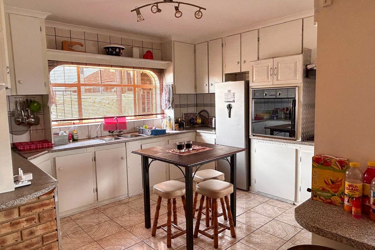 A dated kitchen featuring white cabinetry, built-in oven, tiled flooring, and a large window providing natural light.
