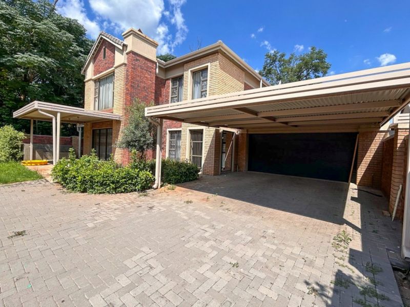 Front exterior view of a double-story brick house featuring a paved driveway, covered carport, and established garden area.