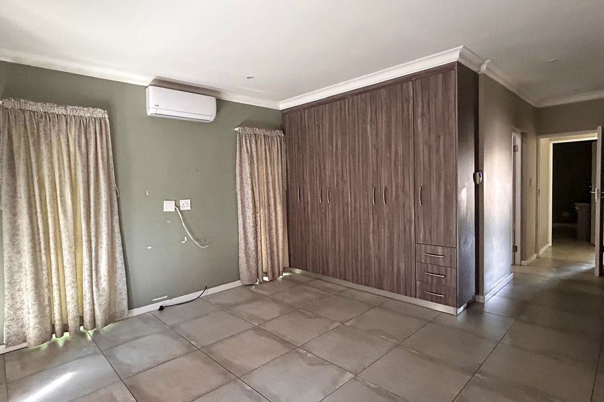 Spacious bedroom featuring built-in wooden cupboards, tiled flooring, and a wall-mounted air conditioning unit.