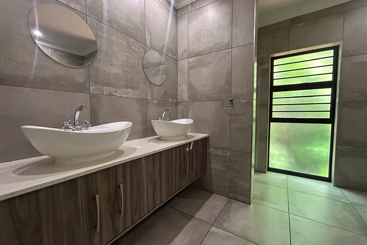 Modern bathroom featuring a double vanity with vessel sinks, large format grey tiling, and a window with security bars.