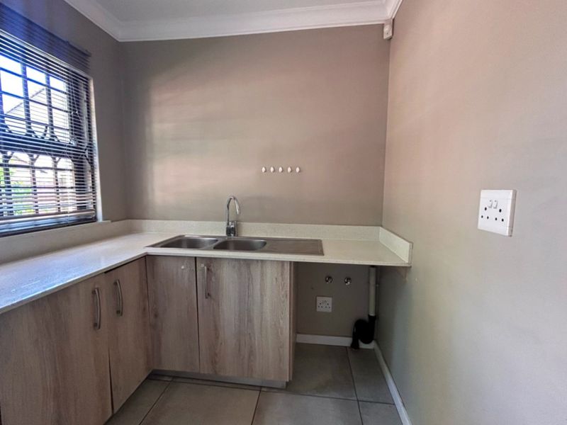 A functional laundry area featuring light wood-finish cabinetry, stone countertops, a double sink, and dedicated plumbing connections for appliances.