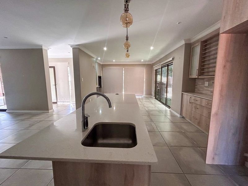 Spacious open-plan kitchen and living area featuring a large island with sink, modern cabinetry, tiled floors, and direct access to the outdoor area.