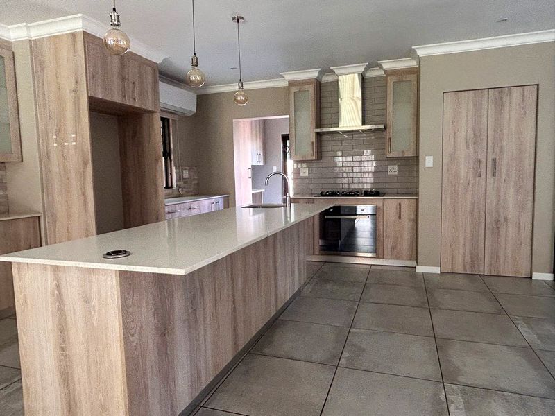 Modern kitchen featuring light wood-grain cabinetry, stone countertops, a central island, built-in appliances, and neutral tiled flooring.