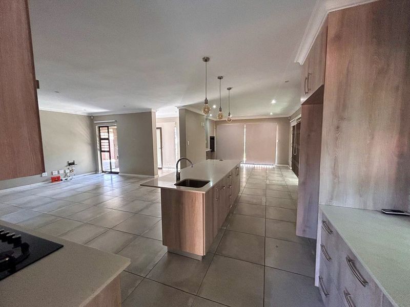 Spacious open-plan living area featuring a modern kitchen with a central island, stone countertops, and neutral tiled flooring throughout.