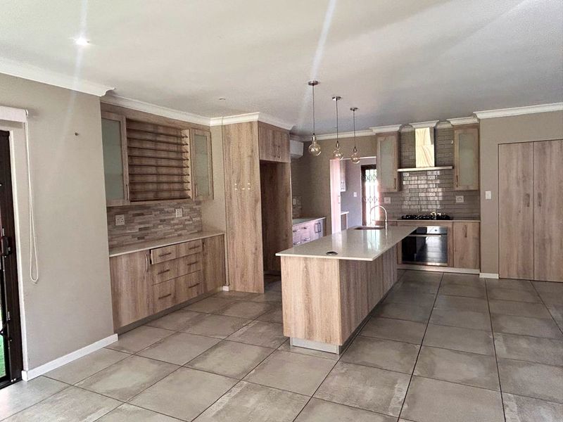 Modern kitchen featuring light wood cabinetry, a central island with stone countertops, built-in appliances, and large format floor tiles.
