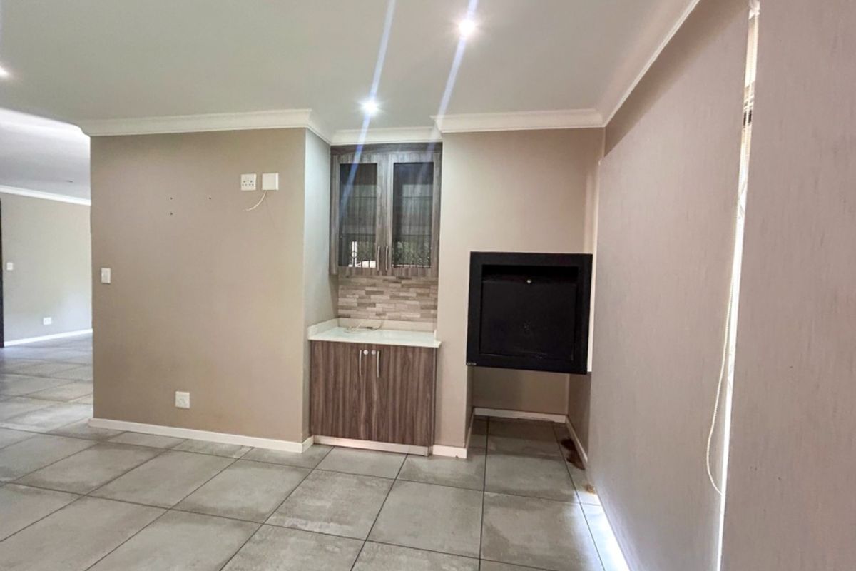 A spacious living area featuring large format floor tiles, a built-in fireplace, and a dedicated cabinetry unit with stone countertop.
