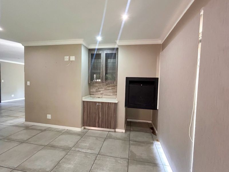 A spacious living area featuring large format floor tiles, a built-in fireplace, and a dedicated cabinetry unit with stone countertop.