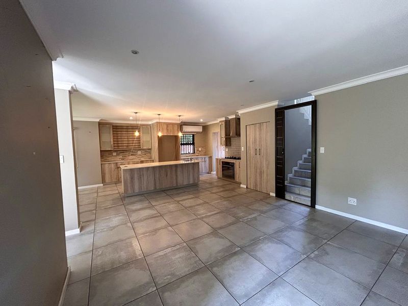 Spacious open-plan kitchen and living area featuring modern wood-finish cabinetry, a central island, tiled floors, and an integrated staircase leading to the upper level.