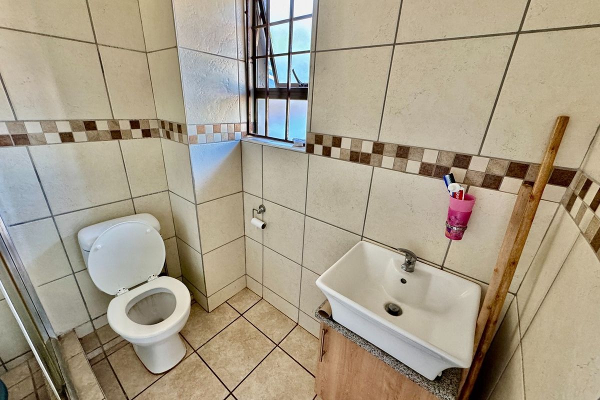 A compact bathroom featuring a wall-mounted basin with vanity cabinet, a standard toilet, and tiled walls with a decorative border.