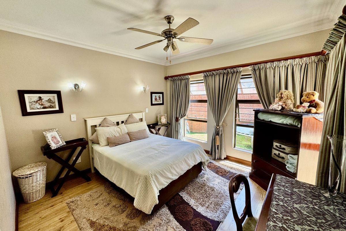 A well-maintained bedroom featuring laminate flooring, a ceiling fan, and large windows with curtain tracks.