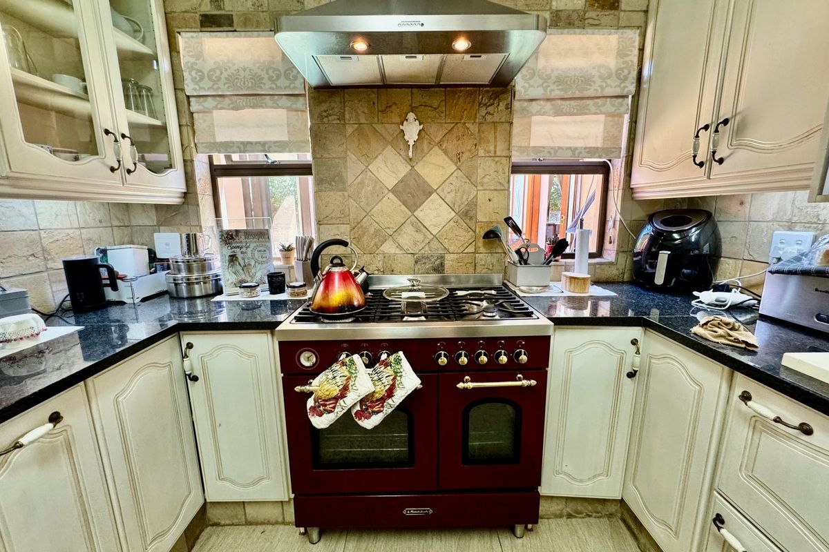 A classic kitchen featuring cream cabinetry, granite countertops, a stone tile backsplash, and a prominent red freestanding gas range with an extractor hood.