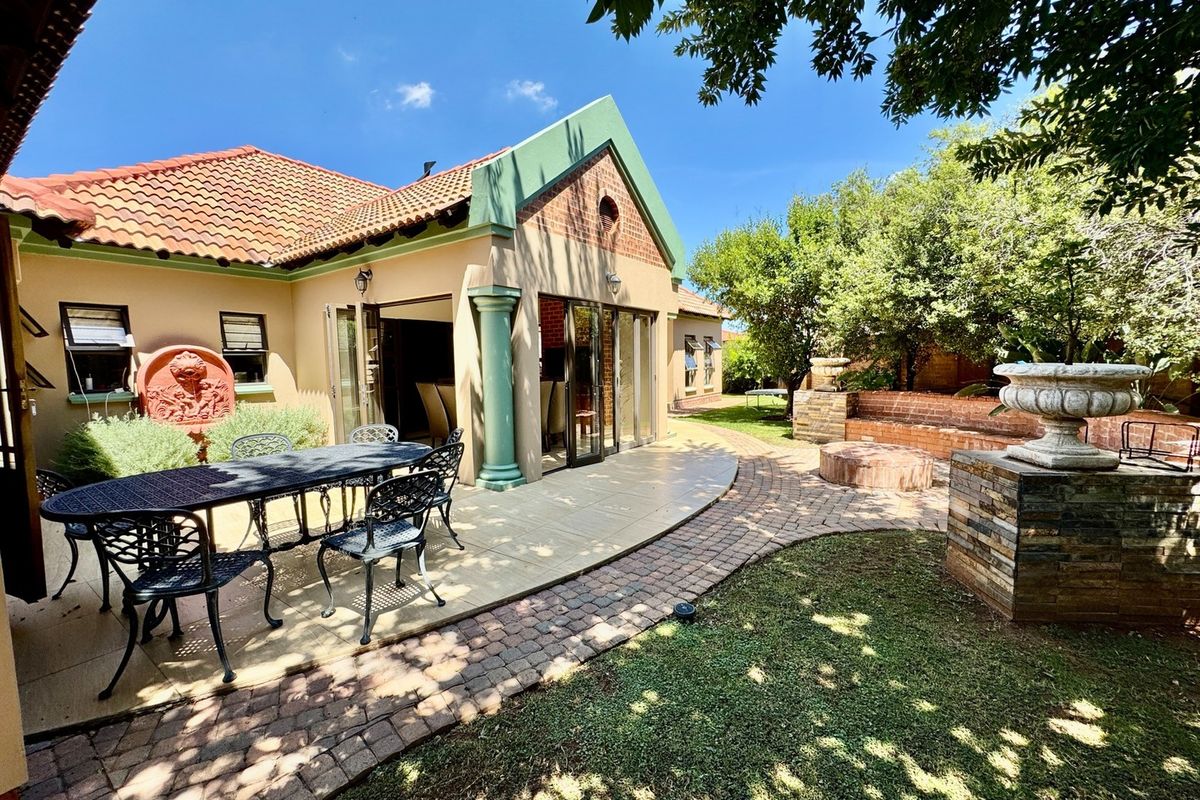 A spacious rear patio area featuring tiled flooring, brick paving, and a landscaped garden with a stone water feature and built-in seating.