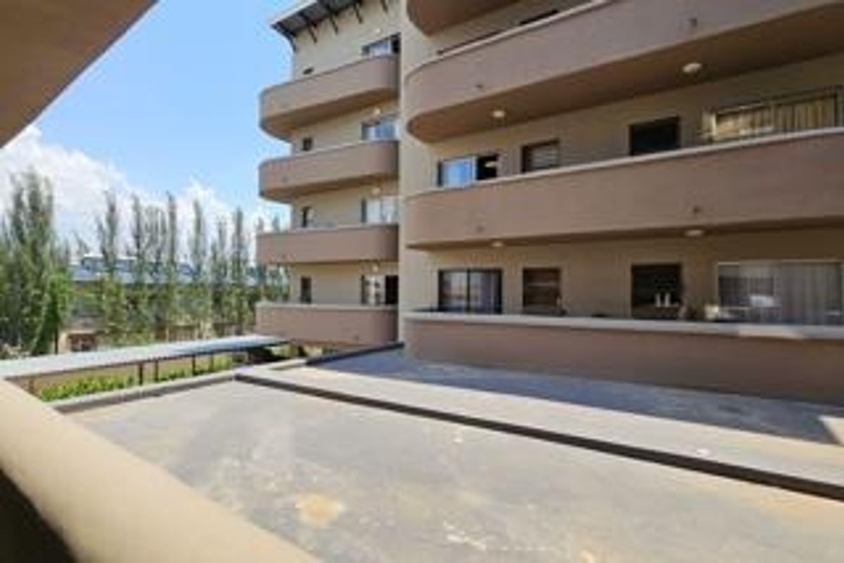 Exterior view of a multi-story apartment building featuring stacked balconies and a large paved terrace area.