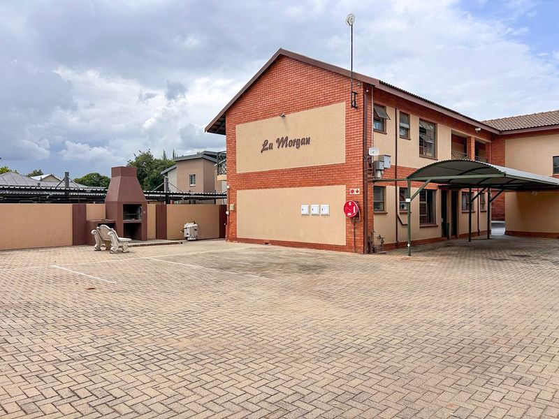 Exterior view of the La Morgan apartment complex featuring paved parking area, covered carport, and a communal built-in braai facility.