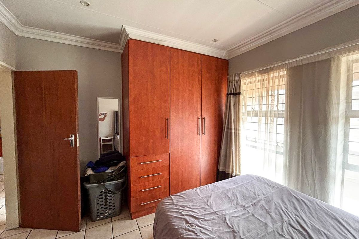 A bedroom featuring built-in wooden cupboards, tiled flooring, and recessed ceiling lighting with security bars on the window.