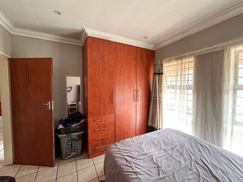 A bedroom featuring built-in wooden cupboards, tiled flooring, and recessed ceiling lighting with security bars on the window.