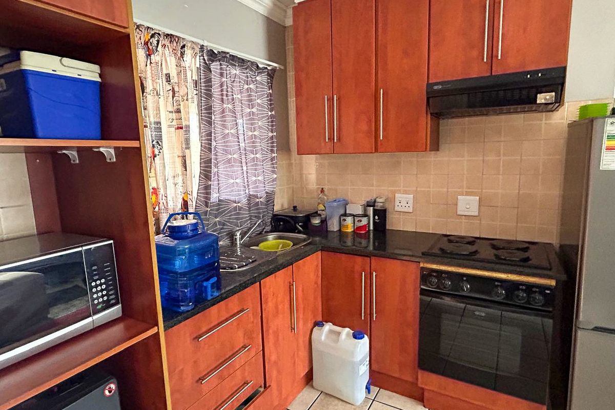 Compact kitchen featuring wood-finish cabinetry, granite countertops, built-in oven, electric hob, and extractor fan with tiled backsplash and flooring.