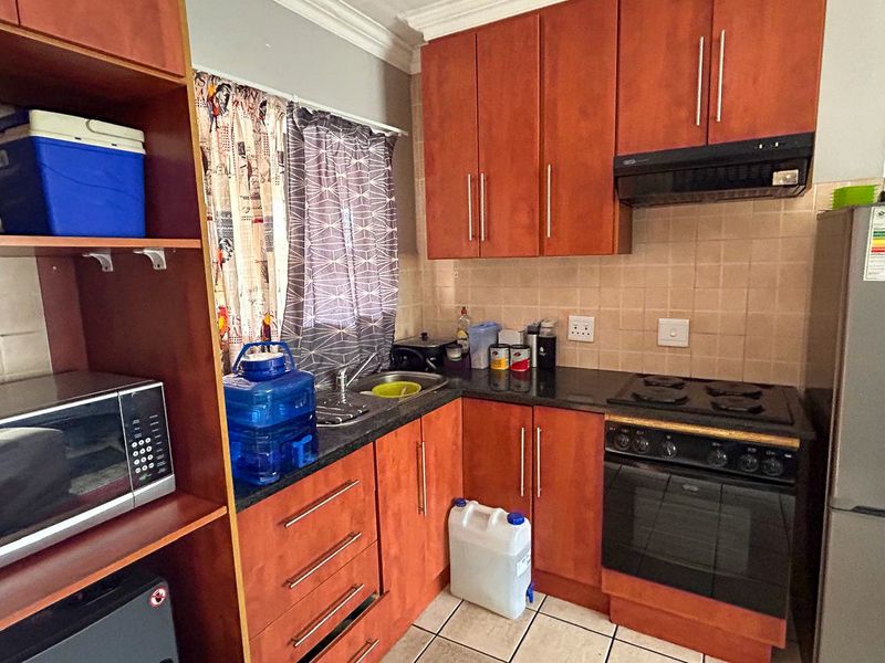 Compact kitchen featuring wood-finish cabinetry, granite countertops, built-in oven, electric hob, and extractor fan with tiled backsplash and flooring.