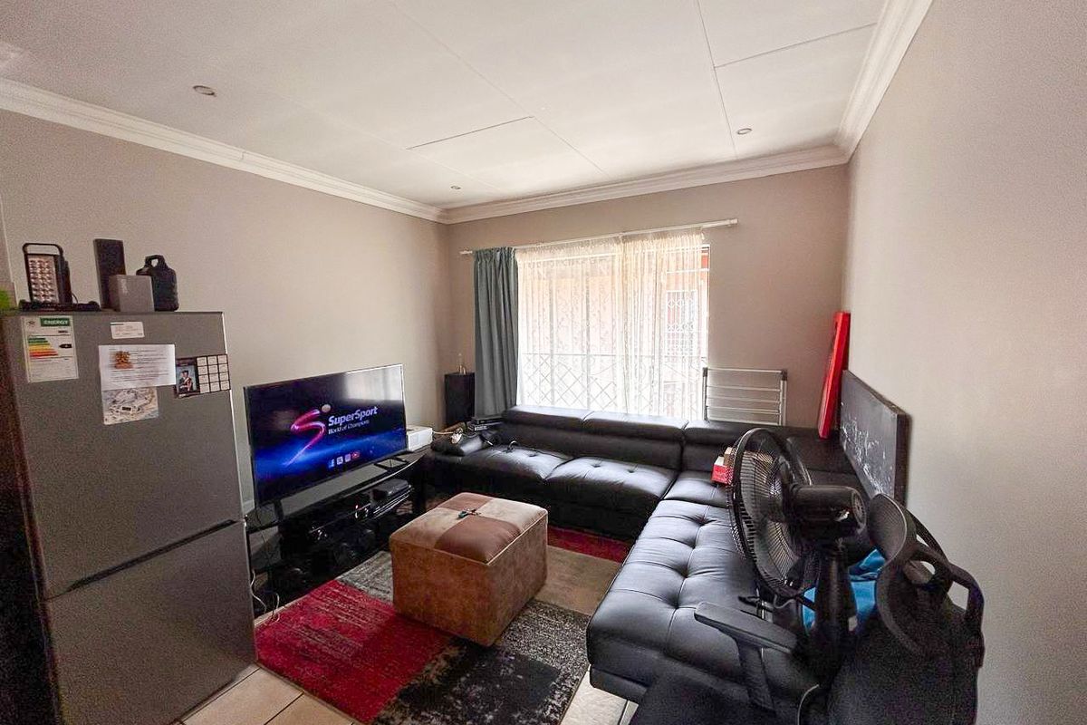 A living room featuring tiled flooring and ceiling cornicing, with access to a window secured by a metal gate.