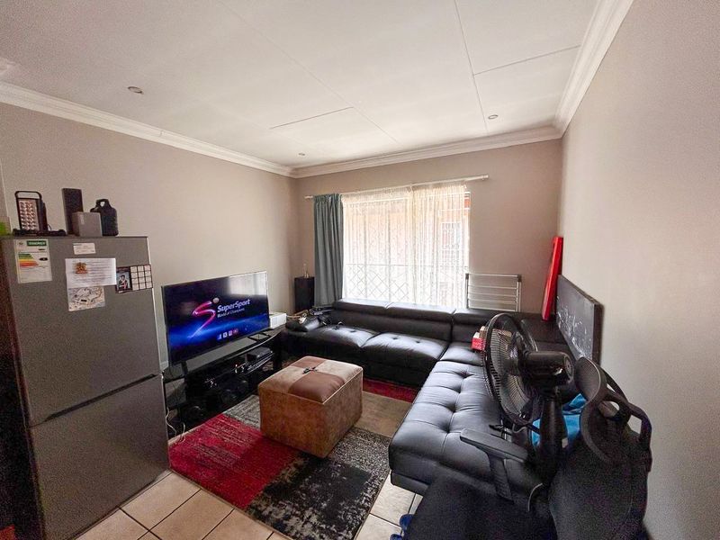 A living room featuring tiled flooring and ceiling cornicing, with access to a window secured by a metal gate.