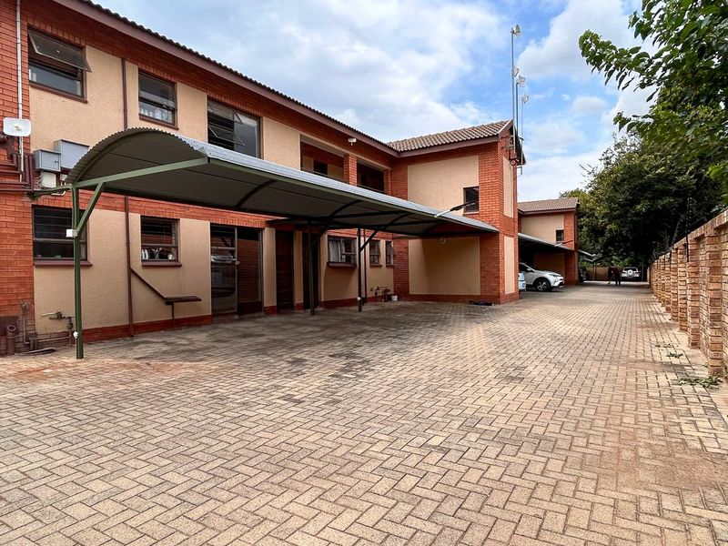Exterior view of an apartment complex featuring a paved driveway, covered parking carports, and a brick facade with perimeter walling.