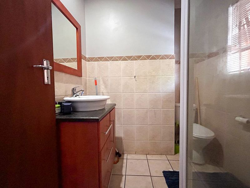 A functional bathroom featuring a vanity cabinet with a countertop basin, a shower enclosure, and a toilet, finished with neutral ceramic wall and floor tiles.