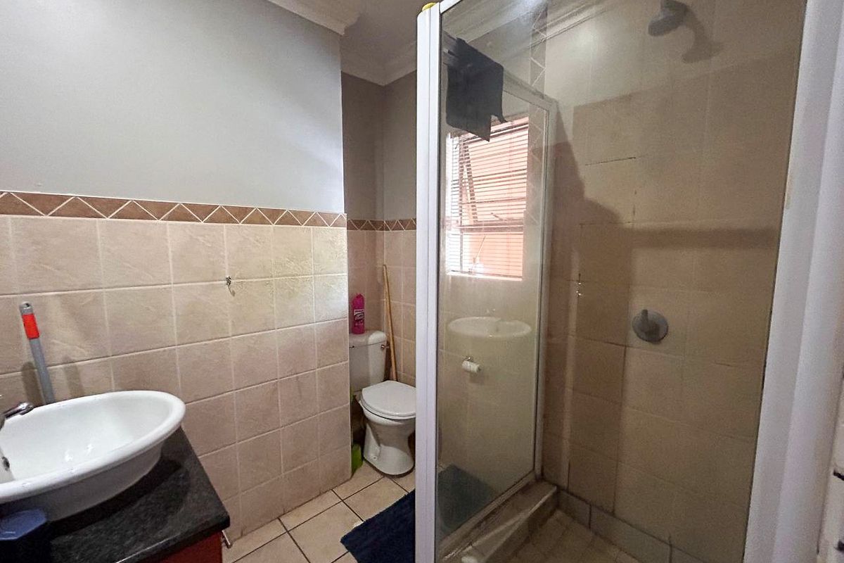 A functional bathroom featuring a shower enclosure, toilet, and a vanity basin with a granite countertop, finished with neutral wall and floor tiling.