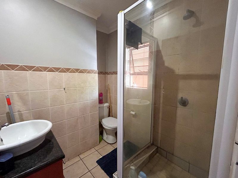 A functional bathroom featuring a shower enclosure, toilet, and a vanity basin with a granite countertop, finished with neutral wall and floor tiling.