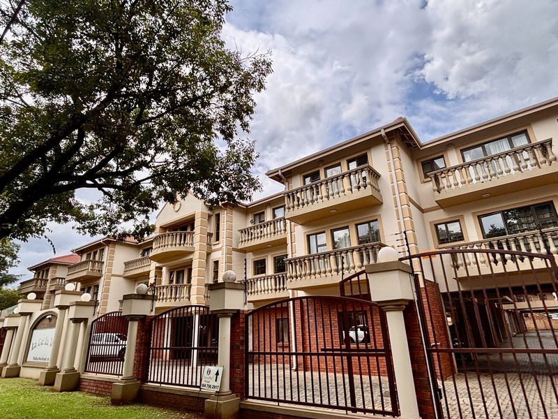 Front elevation of a multi-story apartment complex featuring brick perimeter walls, secure metal gates, and private balconies with classic balustrades.