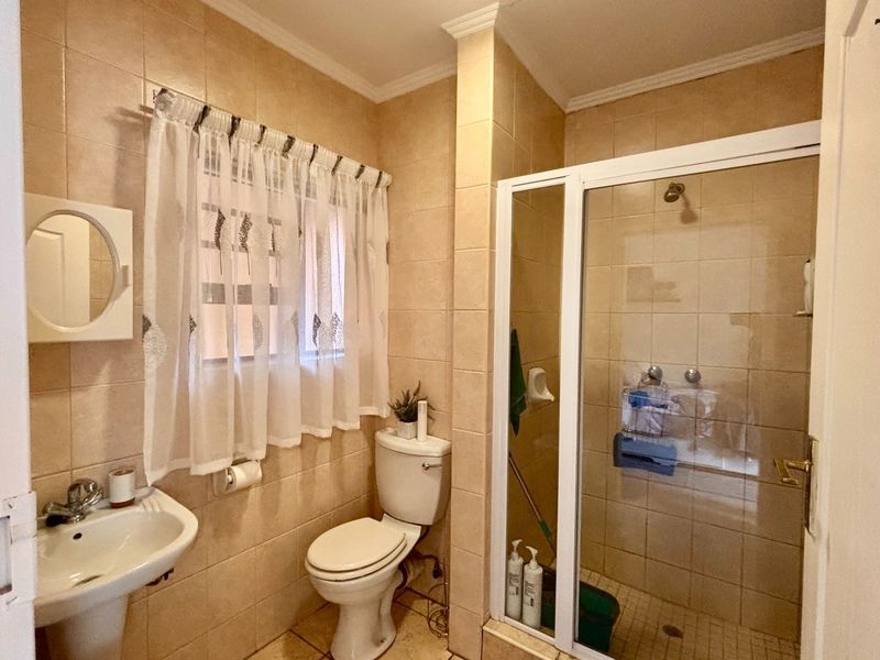 A functional bathroom featuring a pedestal sink, toilet, and a glass-enclosed shower with neutral wall and floor tiling.